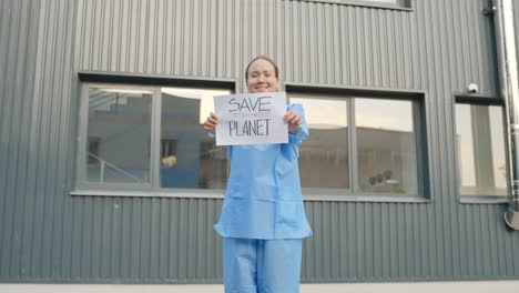 female protester holding a message "save the planet" in front of a laboratory building wearing blue protective outfit