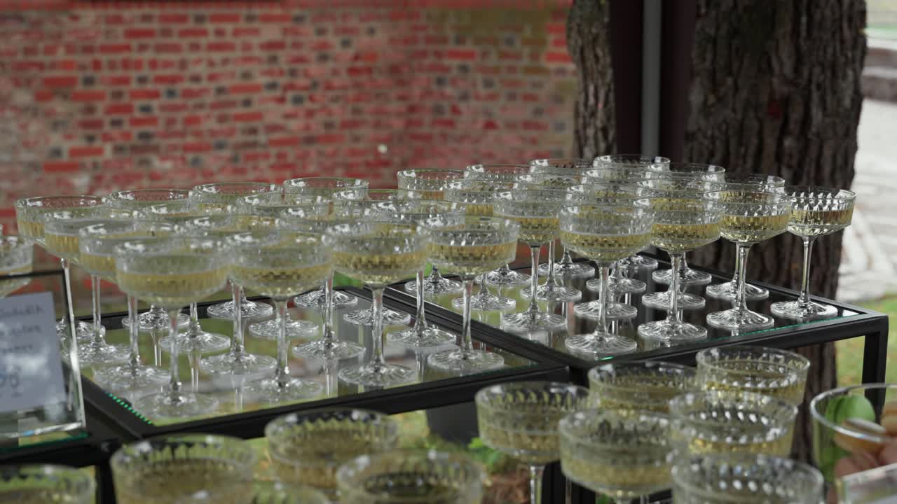 Elegant display of filled champagne glasses arranged neatly on a glass table at an outdoor event, perfect for wedding receptions, toasts, or celebrations