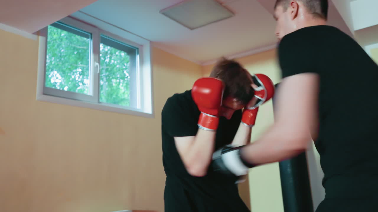 Fighters engaged in sparring session inside gym, young athlete in red gloves defending against opponent attack, practicing martial arts technique, showing concentration, energy, discipline, strength