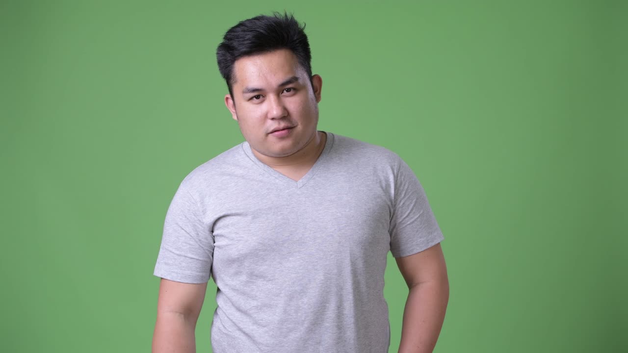 Young handsome overweight Asian man against green background