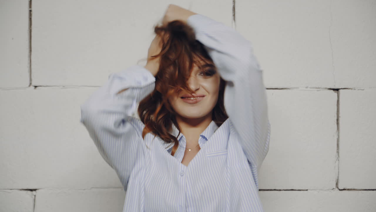 Woman with playful hair in front of a brick wall