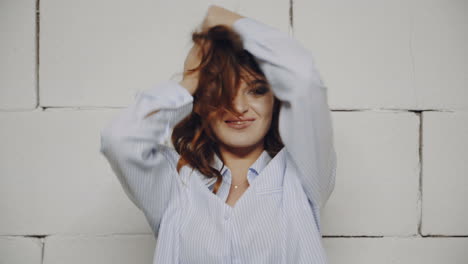 woman with playful hair in front of a brick wall