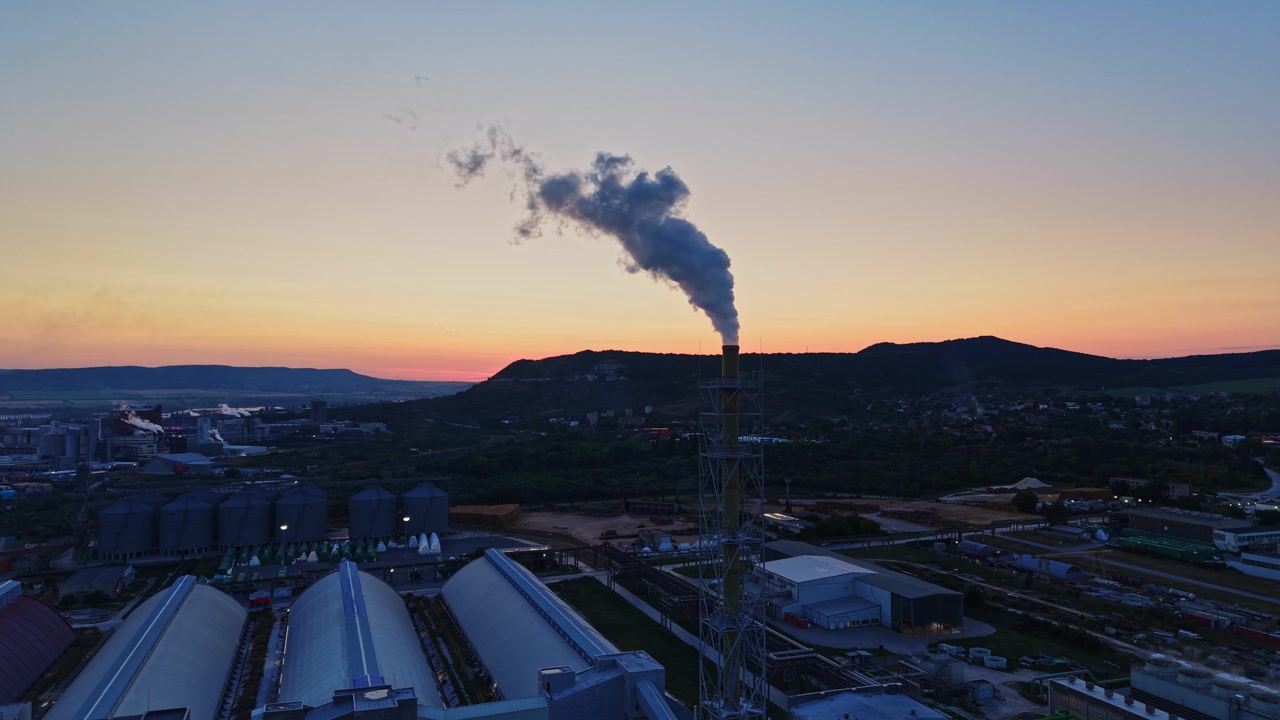 Fumo che sale da una fabbrica al tramonto vicino a un paesaggio rurale.