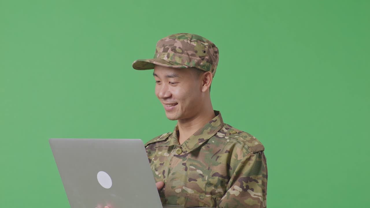 Close Up Of Side View Asian Man Soldier Using A Laptop While Standing In The Green Screen Background Studio