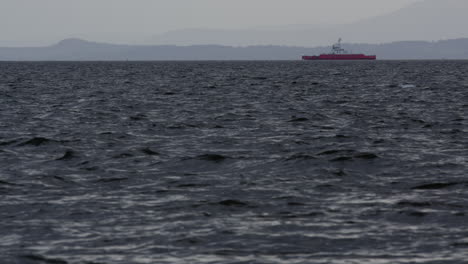 Tug-boat-drives-on-calm-water-in-front-of-mountain-and-forest-haze-backdrop