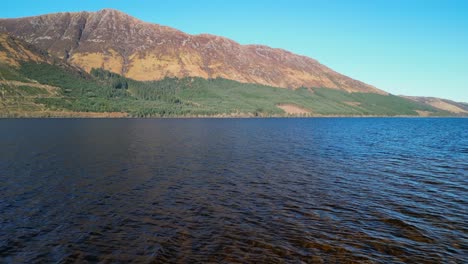 slow low flight over loch lochy towards sunlit mountains in scottish highlands