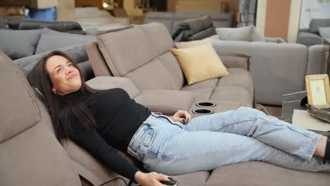 a woman is testing a modern sofa in a furniture store using the remote control for the massage a woman tests a modern sofa in a furniture store using a remote control to check functions such as massage