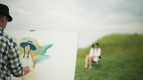 a cartoonist, wearing a hat and checkered shirt, intently paints a portrait on a large canvas in a peaceful grass field. a woman in a hat and white dress is seated in the background