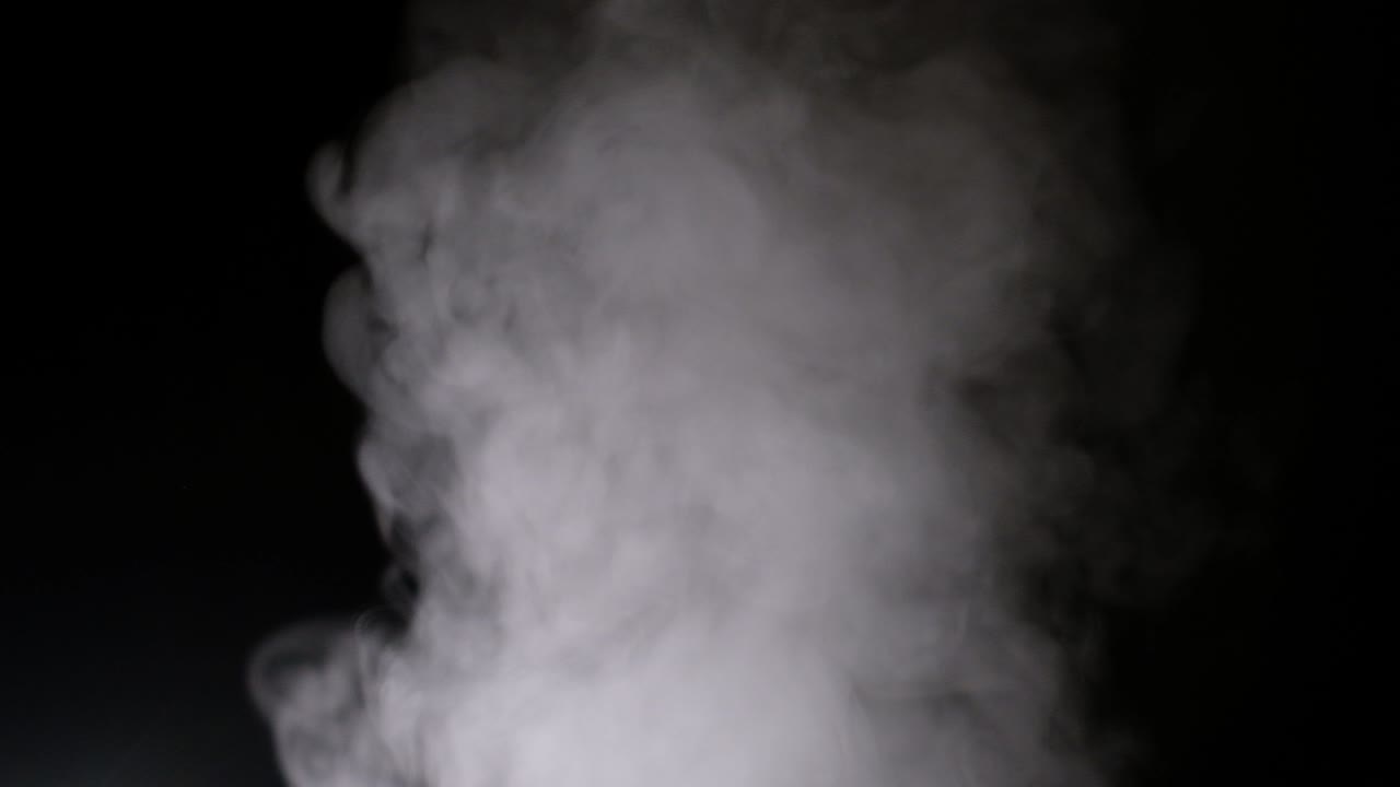 el vapor blanco gira y se eleva desde la sartén. el humo blanco se eleva desde una olla grande, que se encuentra detrás del marco. bucle sin costuras aislado fondo negro.