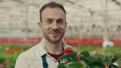 smiling man holding a plant in a greenhouse