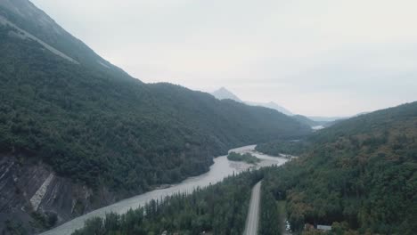 Aerial-view,-drone-flight-along-the-Glenn-Highway-and-the-Matanuska-River-in-the-Chugach-Mountain-Range-of-central-Alaska-on-a-cloudy-summer-day