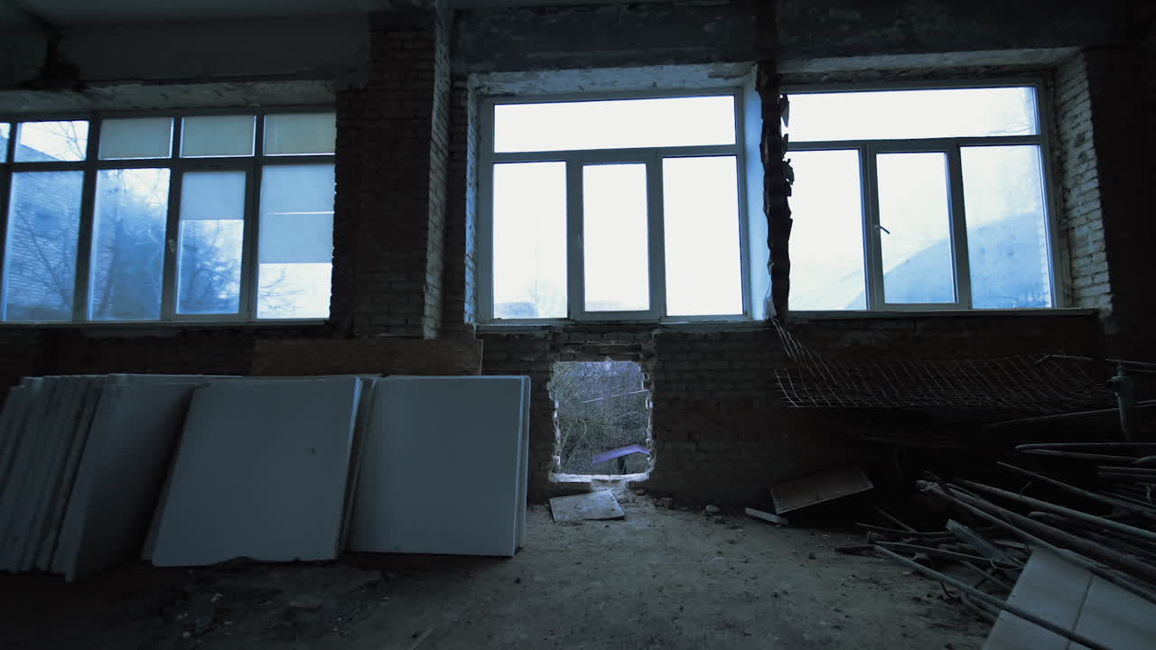Look through the hole in the brick wall on the winter weather outdoors. Big room with some building materials and disassembled scaffolds.