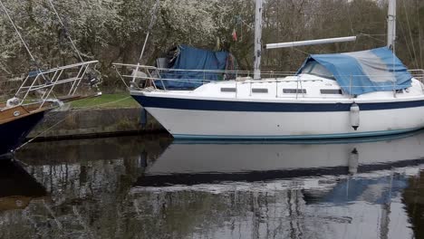 Kleine-Blaue-Segelboote,-Die-An-Einem-Schmalen-Ländlichen-Kanalhafen-Festgemacht-Sind