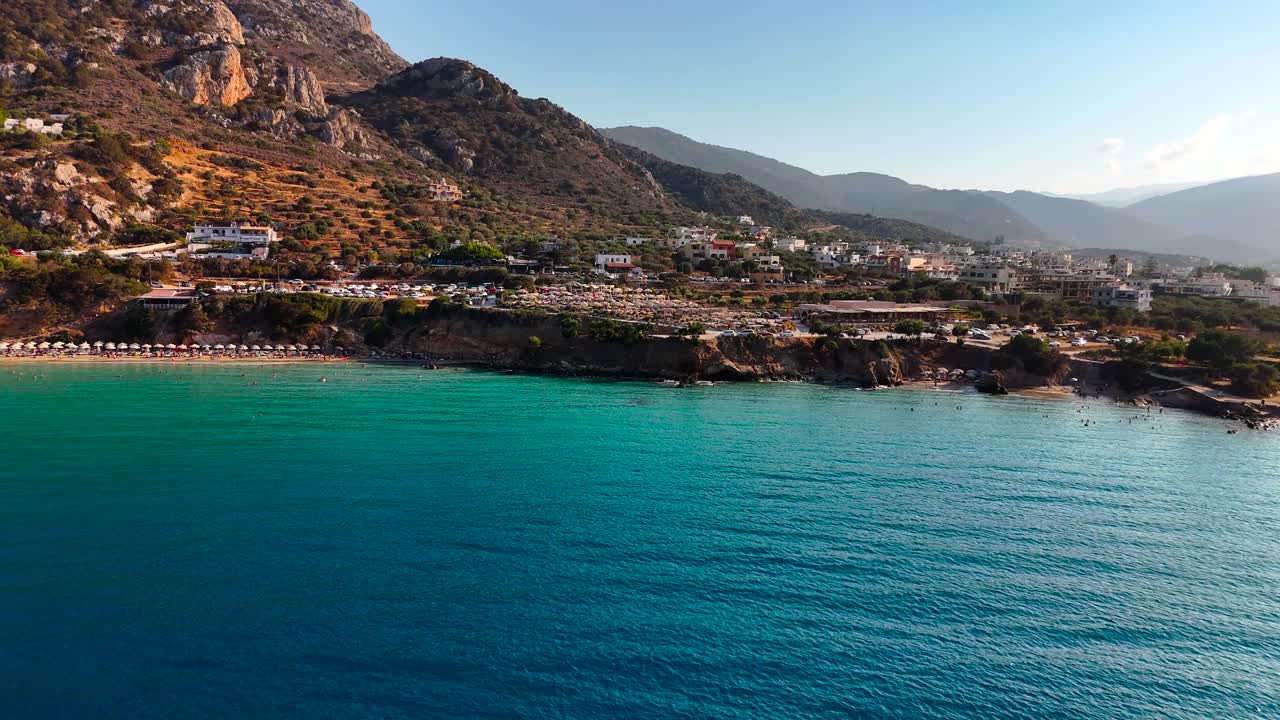 Stunning coastal village offers breathtaking beach views with clear blue waters. The sun shines down on the sandy shore, surrounded by mountains and greenery