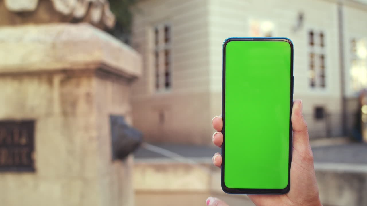 Hand holding a smartphone with green screen in an outdoor setting