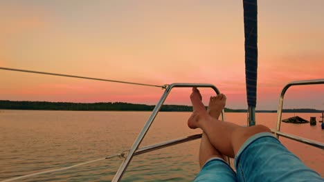 man legs laying and relaxing on the sail boat deck alone with sunset in background - concept of travel people and freedom in summer holiday vacation