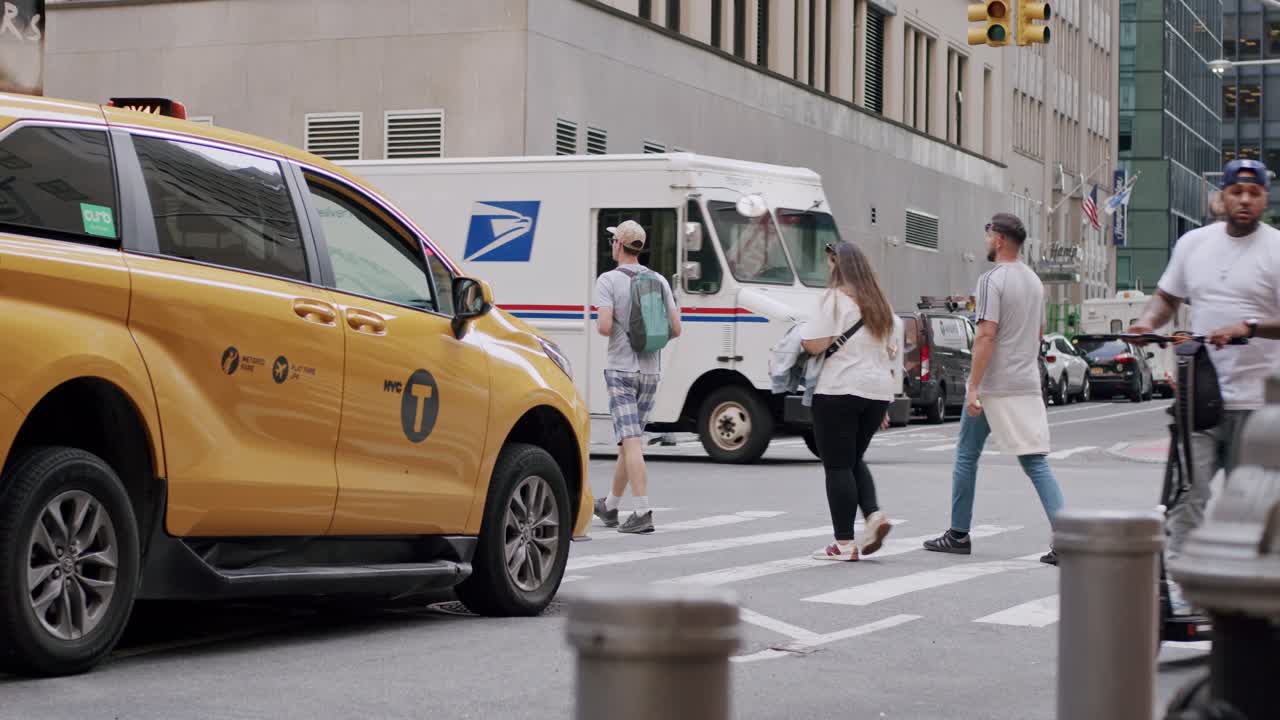 A New York City taxi waits as pedestrians and cyclists move through a busy urban street intersection