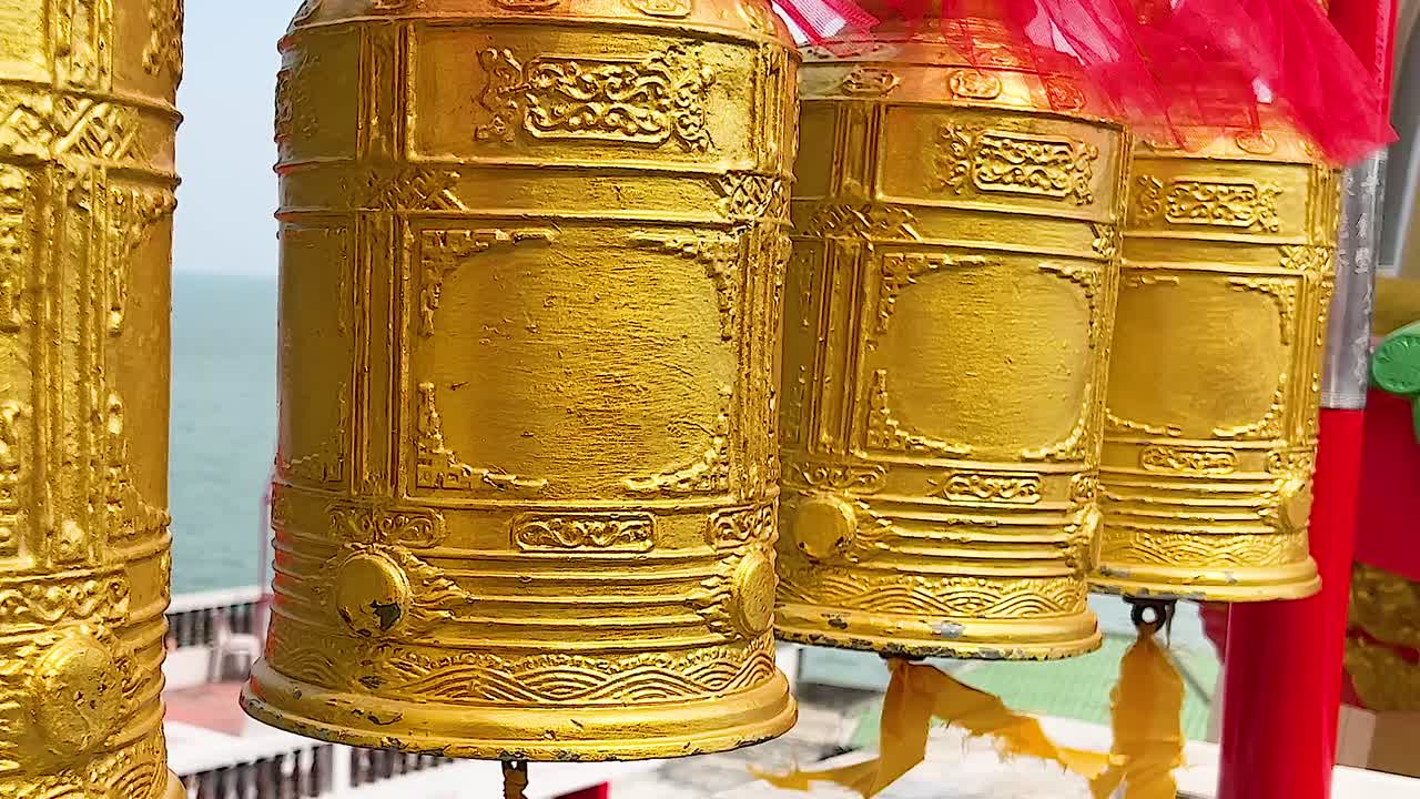 Close-up view of ornate golden prayer wheels with a seaside backdrop.