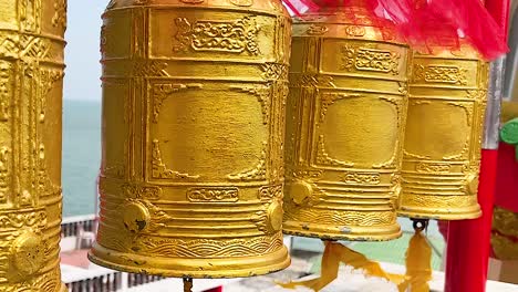 close-up view of ornate golden prayer wheels with a seaside backdrop.