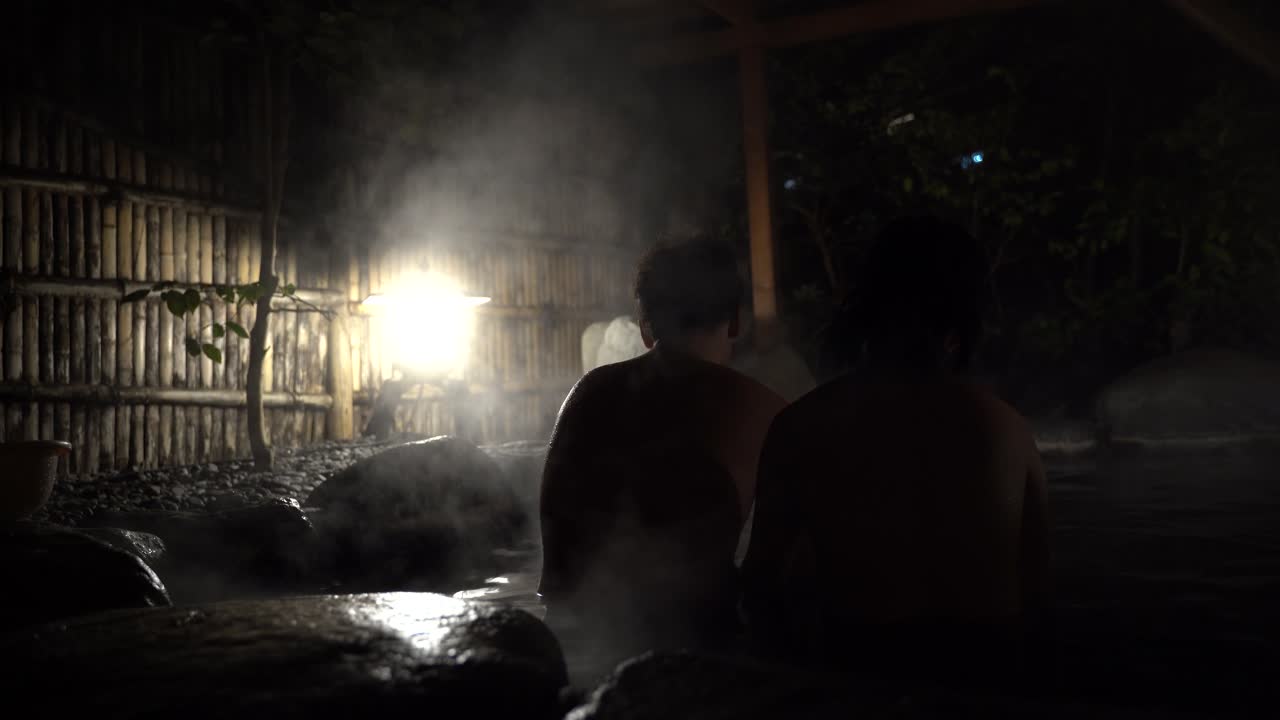 Silhouette of couple sitting inside outdoor Onsen,Japanese hot spring bath