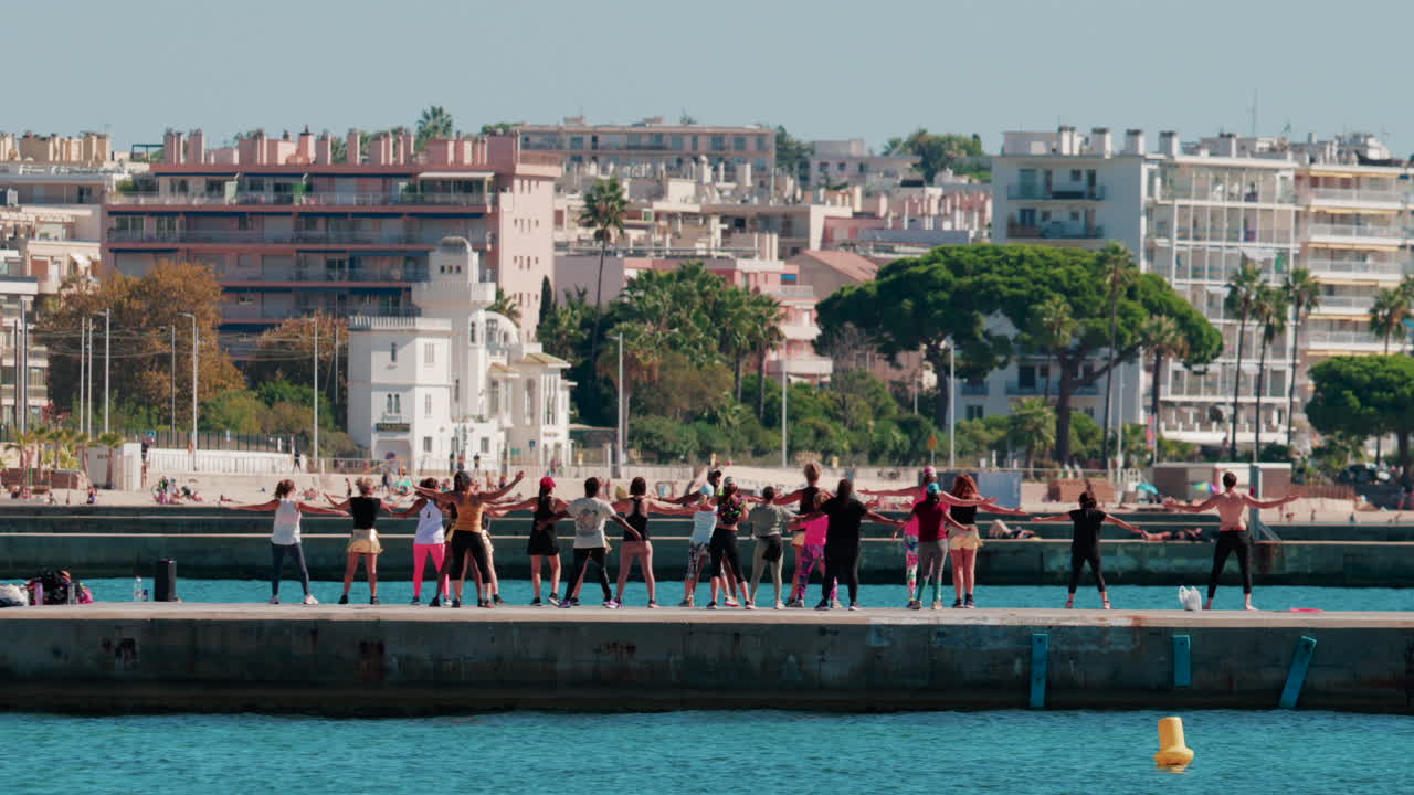 Cannes, France - October 7, 2025: A group of people practicing dance or fitness on a pier by the sea on a sunny day