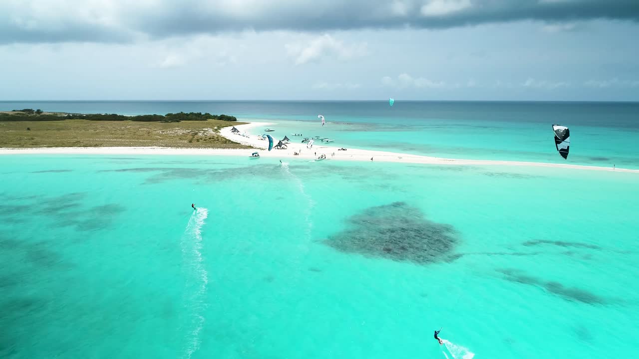카이트 서퍼 들 은  ⁇ 은 파란 바다 물 에서 하늘 에 날아다니며  ⁇  모래 해변 에 날아다닌다