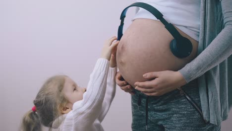 el niño acaricia el abdomen de la madre embarazada con auriculares en la habitación