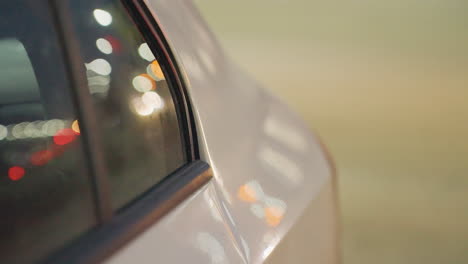close up side view of parked car under night streetlight, showing blurred reflections of cars moving behind, captured through smooth glass window with bokeh glow and subtle vehicle outlines