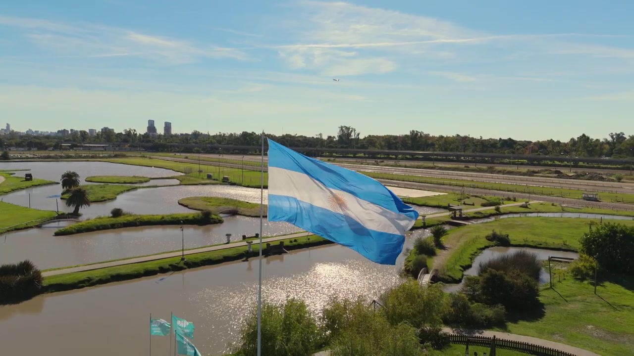 Drapeau argentin flottant sur un grand mât au bord de l'eau avec des vues sur un parc et la ligne d'horizon de la ville