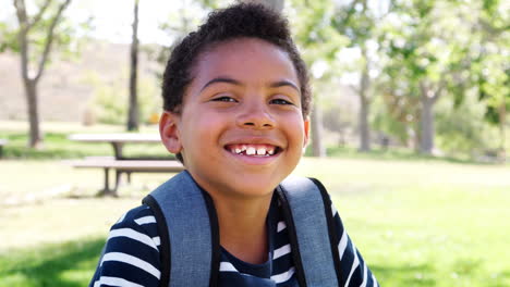 retrato en cámara lenta de un niño con una mochila en el parque sonriendo a la cámara