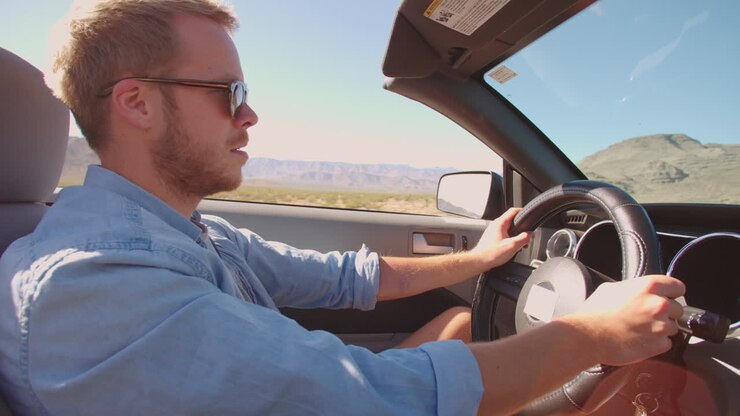 Uomo in auto decappottabile che guida lungo una strada aperta ripreso con R3D