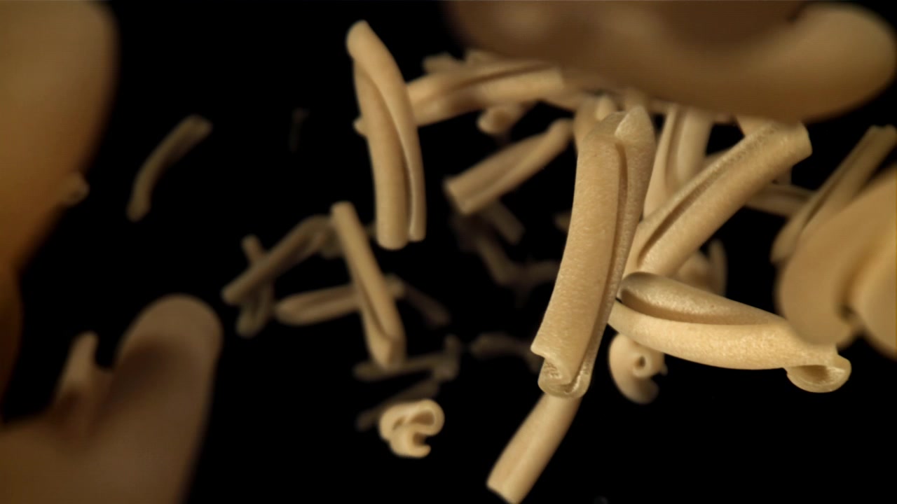 Pasta casarecce cruda che cade al rallentatore su sfondo nero.