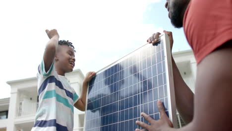 african american father and son handle a solar panel outdoors at home