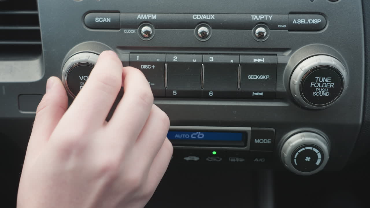 Close up of person pressing volume push and turning knob on car audio control panel interior focusing on finger interaction with rotary dial and media power function in modern vehicle cabin