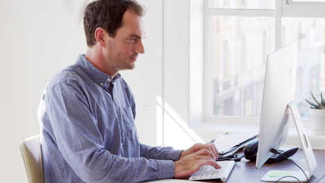 Young-white-man-using-phone-and-computer-in-an-office