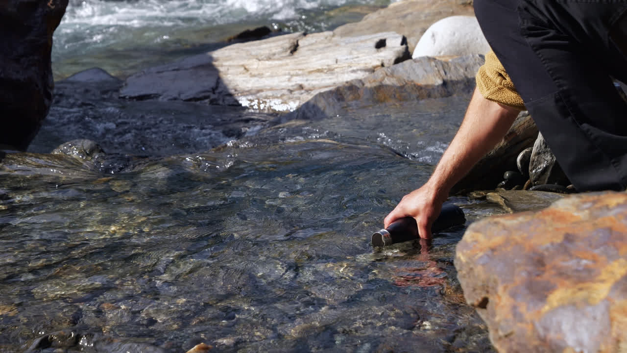primer plano de un excursionista llenando una botella con agua dulce natural en una corriente fluvial