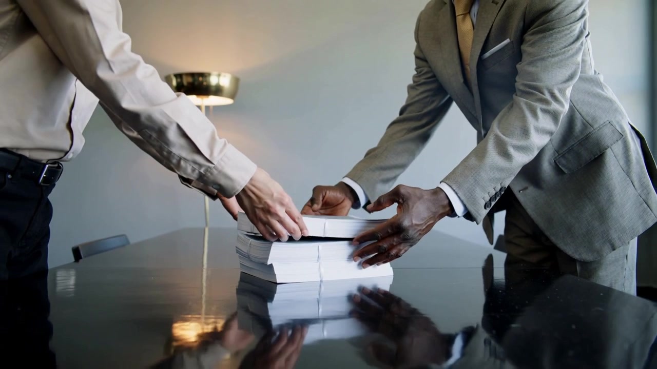 Placing suit-clad men aligning paper stacks on conference table as colleague handing for meeting
