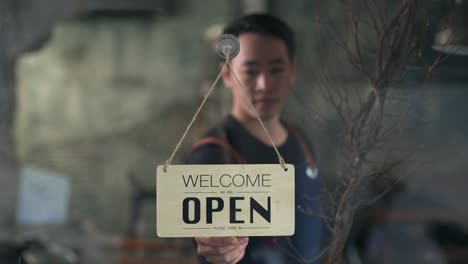 4k asian man coffee shop owner turning hanging closed sign to open on the door