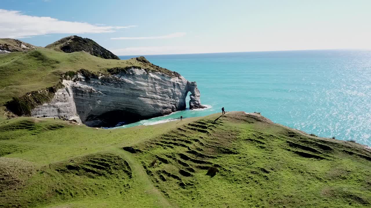 Aerial drone shot flying over a coastal cliff path with hikers on a sunny day