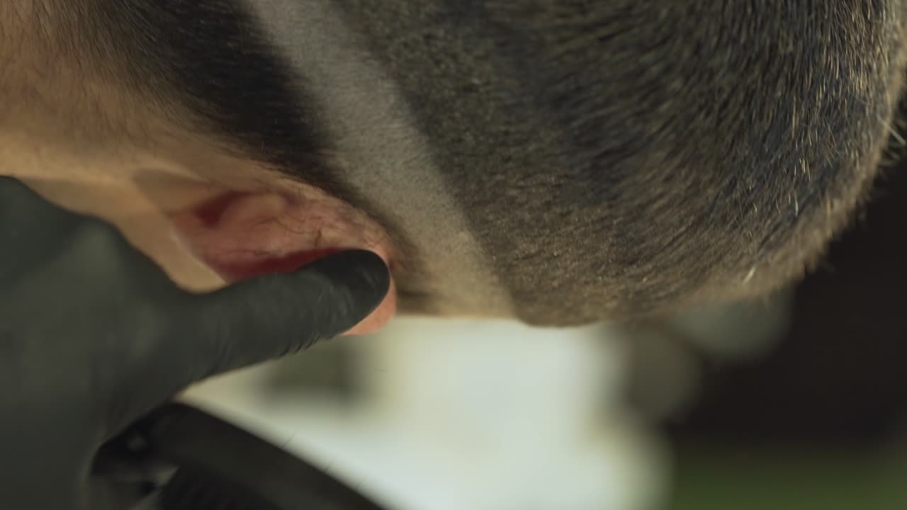 이발기의 도움으로 이발사는 고객의 머리를 측면에서 다듬고 머리 디자인을 위해 귀 위에 큰 선을 만듭니다.