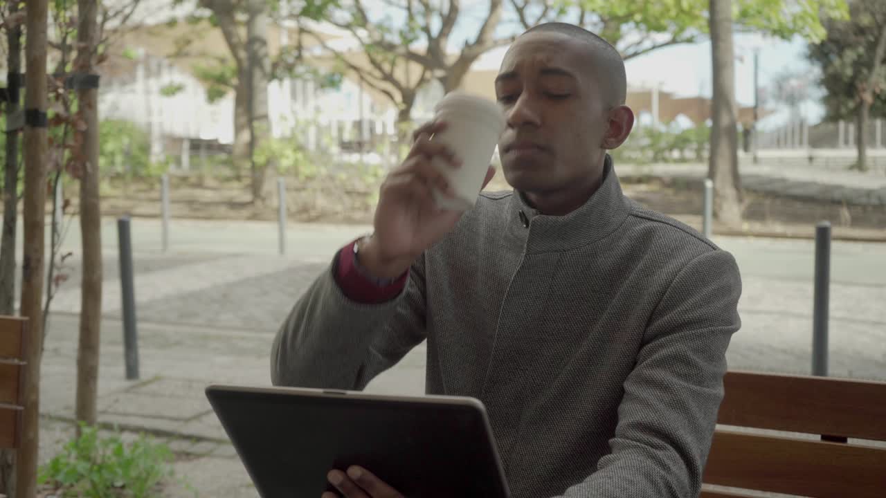 Serious man using digital tablet and drinking coffee to go