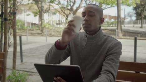 hombre serio usando una tableta digital y bebiendo café para ir