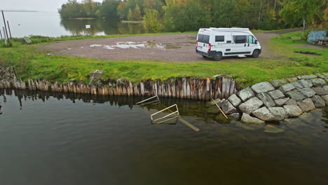 white van parked by the calm lakeshore with autumn trees in the background in sweden