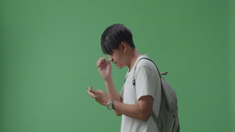 화가 난 아시아 남성 학생이 모바일 게임을 하고 녹색 스크린 스튜디오에서 는 동안 패배합니다.