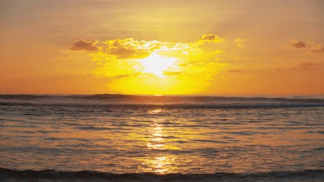 Bright-golden-sun-setting-behind-ocean-with-powerful-waves,-slow-motion-shot