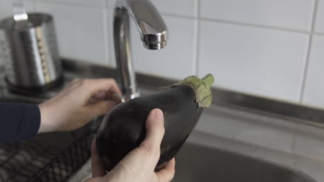 slow-motion shot as opening the tap, washing eggplant with water in the kitchen