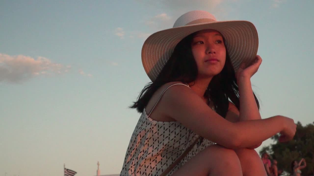 작은 그리스 국기와 구름을 배경으로 거리를 바라보며 여름 모자를 쓴 소녀