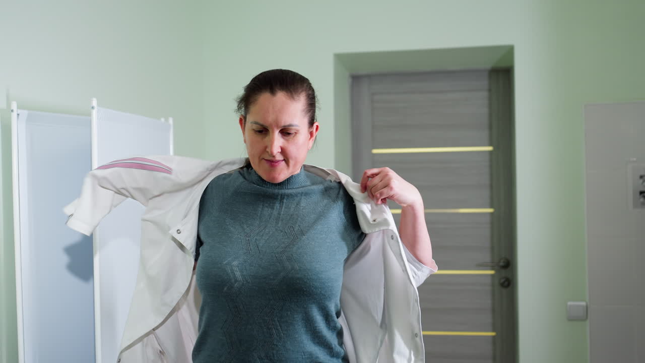 Close up of nurse putting on work cloth with smile on face preparing for day inside bright clean clinic, symbolizing readiness, dedication, and professionalism in healthcare environment