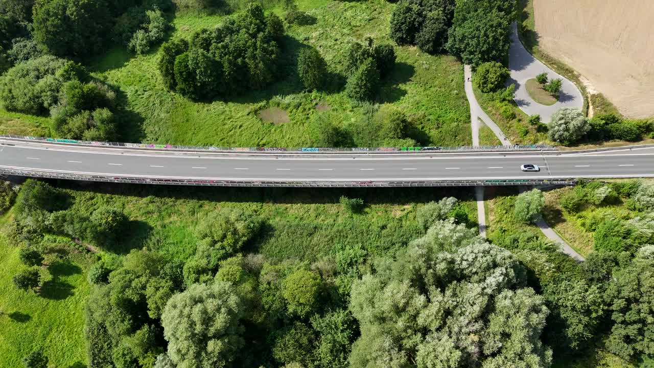 Aerial tracking shots of cars on rural suburb highway in American countryside. Bright sunny day in USA. Green forest landscape and Farm fields. Top down shot