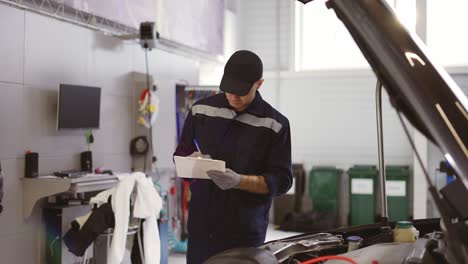 mechanic in a auto repair shot checking engine making notes to his tablet